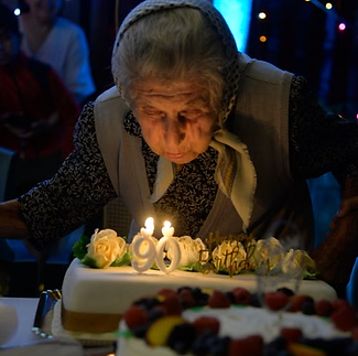 Starija žena duva svećicu na torti za svoj 90. rođendan