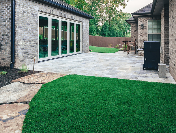 Patio surrounded by turf between a home and outdoor pavilion.
