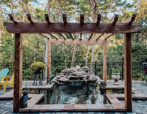 Pergola covering koi pond with boulder and stone water feature.