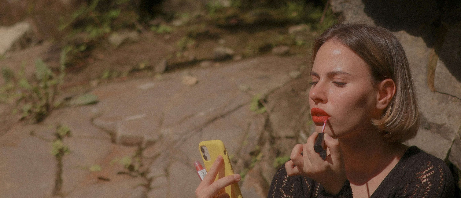 femme sui se met du rouge à lèvre devant son téléphone portable jaune