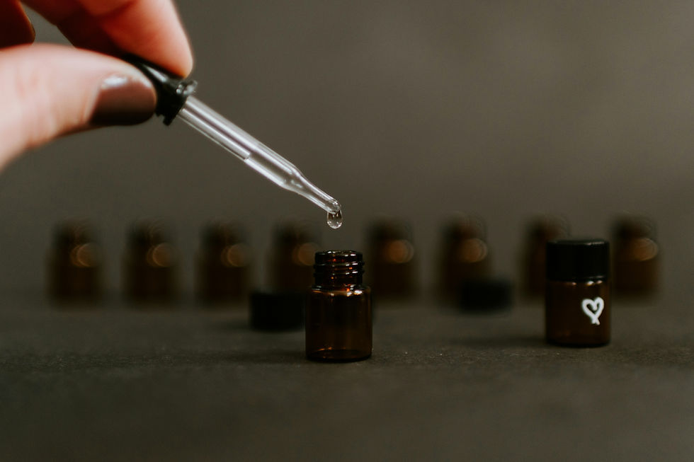 une main de femme tient une pipette dans laquelle une goutte d'huile essentiell est en train de tomber dans un flacon marron opaque