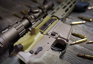 Close-up of a custom Cerakote AR-style rifle featuring bronze, tan, and OD green earth-tone finishes with a mounted scope.