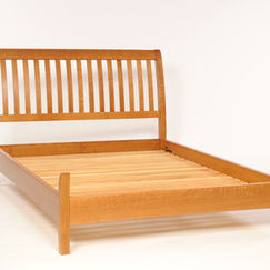 A simple white oak bed with a curved headboard. 