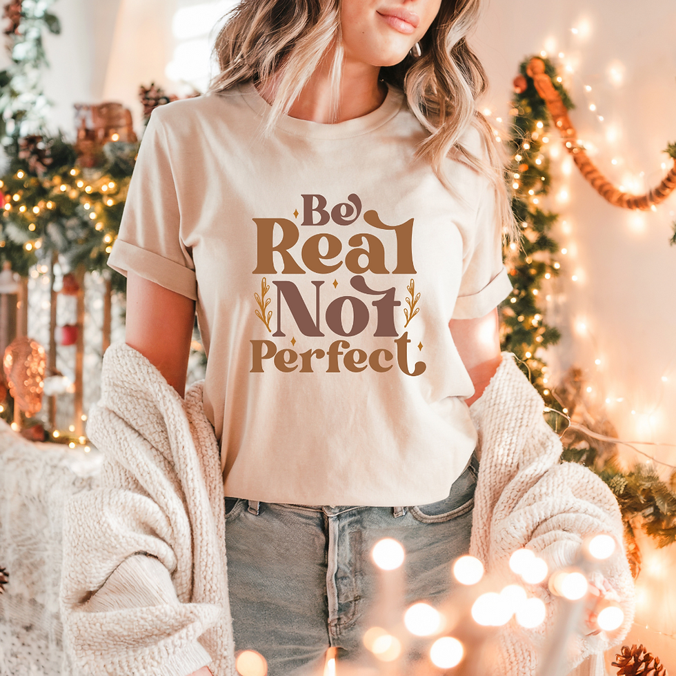 Young girl wearing a white short-sleeve T-shirt with the phrase 'Be Real, Not Perfect' in bold brown letters, promoting authenticity and self-acceptance.
