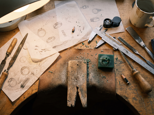 Graphite ring sketches, calipers and wax-carving tools laid out on a jeweler’s bench