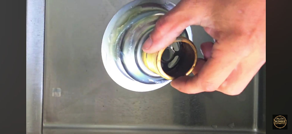 Removing old silicone from a stainless steel sink drain with a blade.