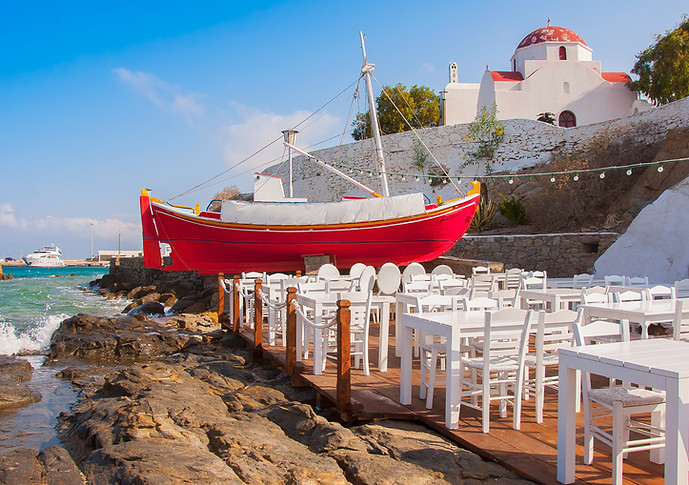 The famous red boat and tables and chairs of Baboulas' taverna, Mykonos., Greece