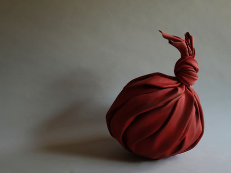 陶芸家・田中悠による、布で何かを包んだような赤い陶作品《tsutsumimono》