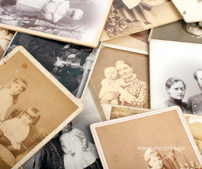 Alte Familienfotos, verstreut auf einem Tisch, die die Vergangenheit und die Ahnen symbolisieren, die oft im Kontext von Generationstrauma eine Rolle spielen.