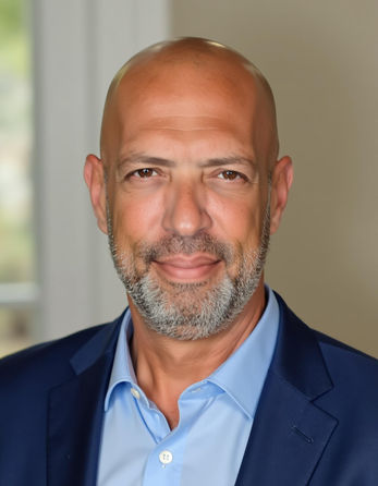 גבר מזוקן מחייך, לובש חליפה כחולה, מביט ישירות למצלמה, Smartshot Ai.