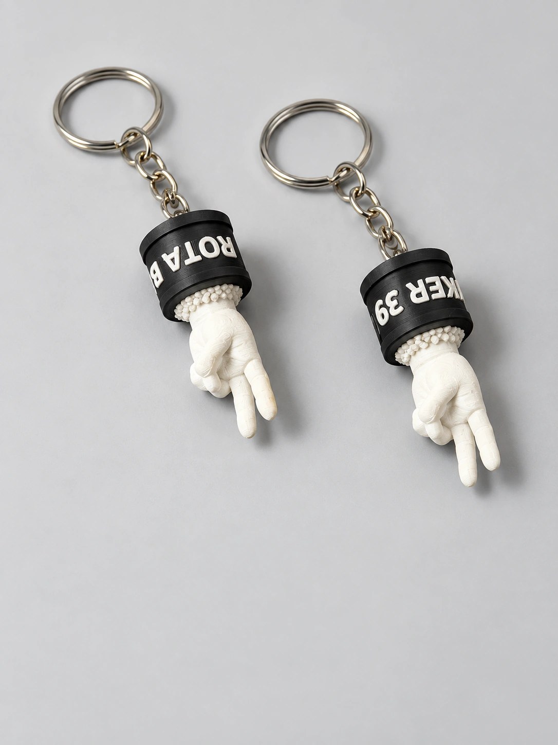 Dupla de chaveiros Rota Biker 39 com base preta, mão branca e argola de metal em fundo claro