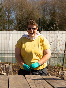 A laughing person with short brown hair. They are wearing a yellow tshirt and green gloves