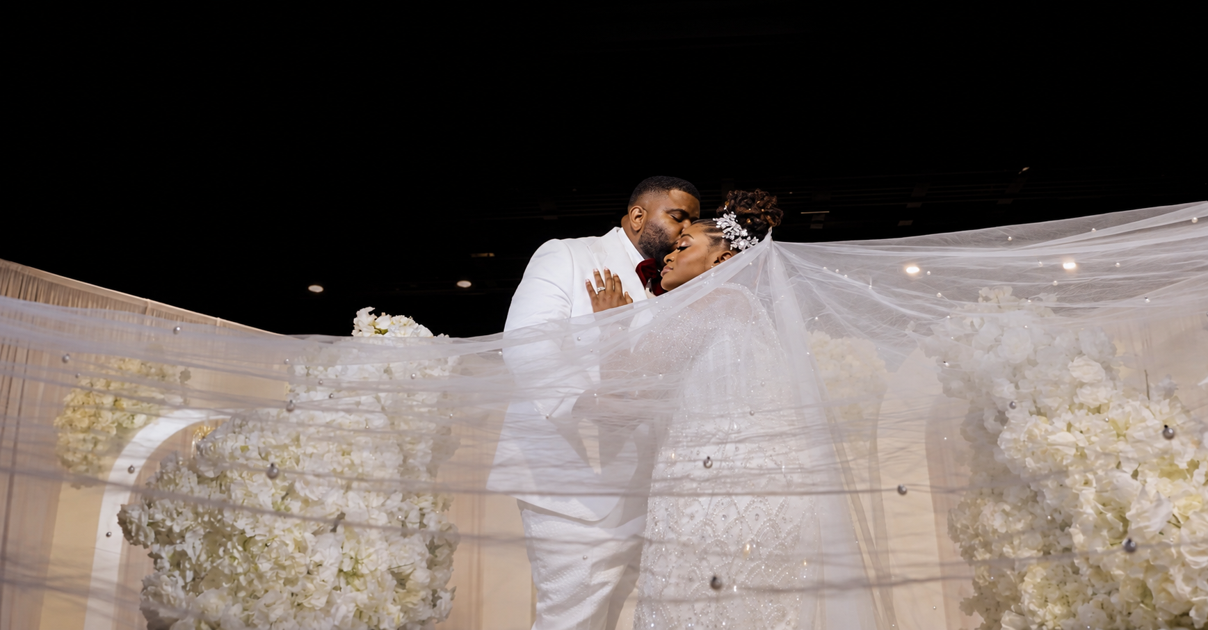 Bride and groom kissing beneath a softly spread translucent wedding veil