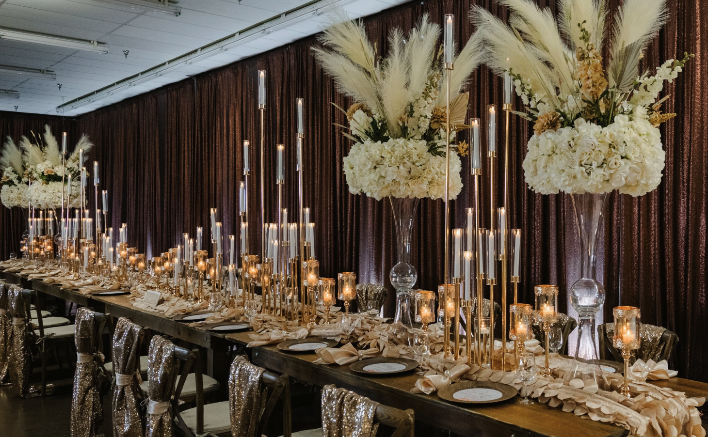 Wedding reception table with ivory flowers, tall candles, gold accents, and textured draping