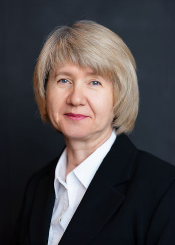 Blonde Geschäftsfrau in weißer Bluse und schwarzem Blazer lächelt freundlich.