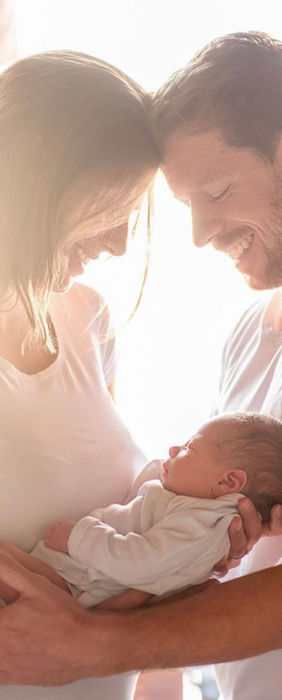 Eltern wiegen zärtlich neugeborenes Baby, Köpfe berühren sich liebevoll.