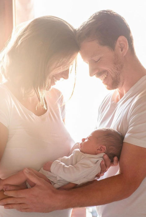 Glückliche Eltern halten zärtlich ihr neugeborenes Baby, Köpfe sanft berührend.
