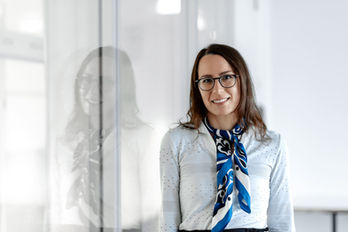 Lächelnde Frau mit Brille und blauem Schal im modernen Büro.