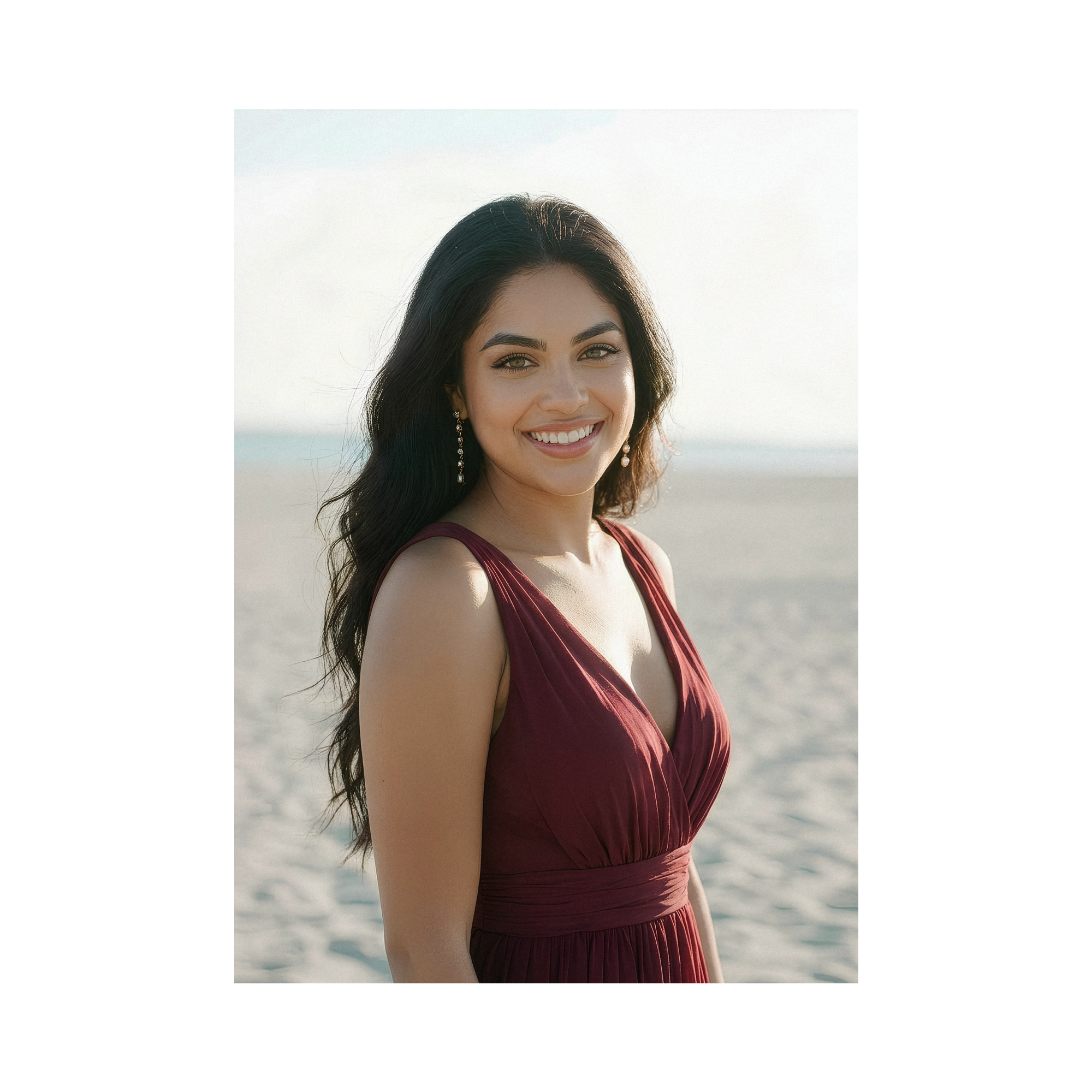 A soft-toned photo of Judith smiling at the camera, her green eye sparkling in front of the ocean wearing a burgundy dress