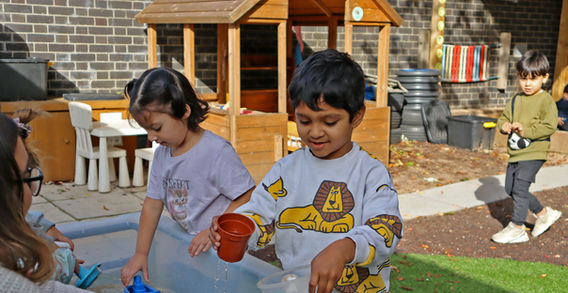 Children playing with water and toys outdoors with a wooden playhouse in background