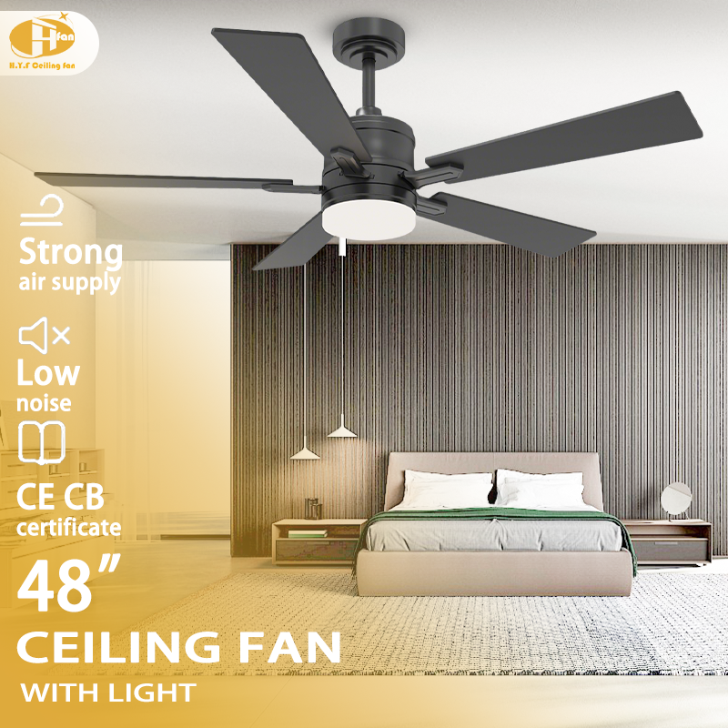 Black ceiling fan with light for bedroom, five plywood blades and a round lamp pictured above a bed.