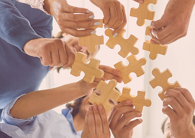Foto de baixo para cima mostrando as mãos de várias pessoas segurando peças de quebra-cabeça de madeira