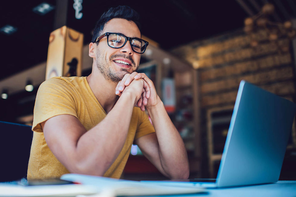 A business owner resting his chin on his hands and smiling at the camera in front of a laptop computer