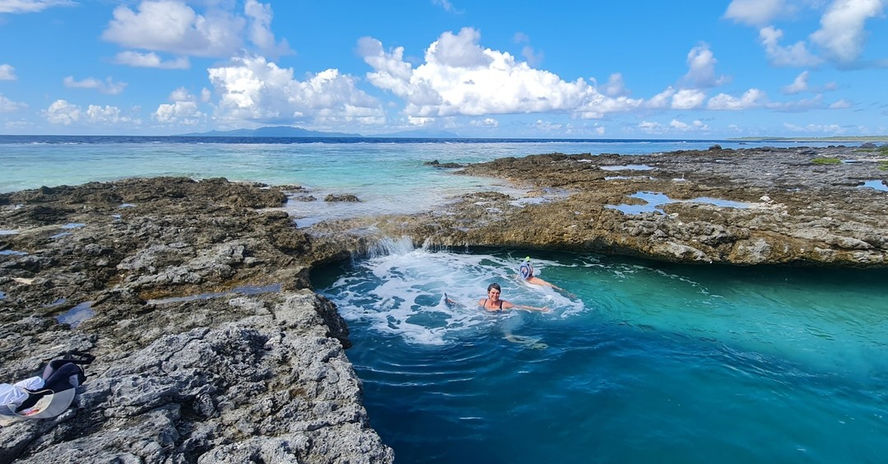 Two people swimming in a turquoise pool near a rocky coast.