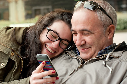 Father and daughter hugging smiling and looking at mobile phone: The Parents' Guide to