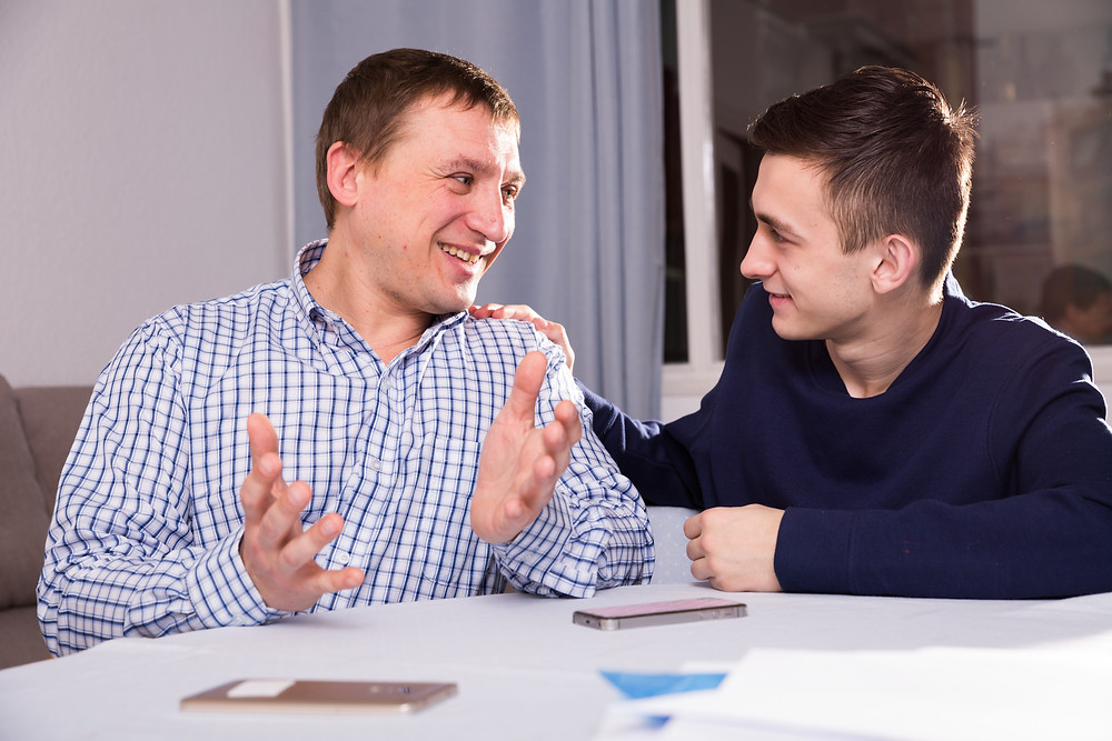 Father and teenage son in kitchen talking anxiety smile The Parents' Guide to