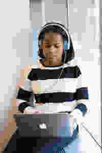 Femal teen student sitting and listening to a podcast with headphones and a laptop