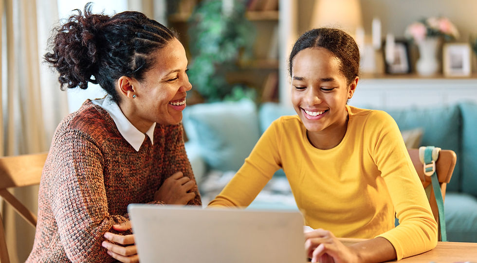 Mother and daughter smiling and looking at a laptop in a cozy room. One wears a yellow shirt, the other a brown sweater. Bright, warm atmosphere.