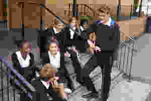 Group of secondary school students sitting on stairs of the entrance to school chatting