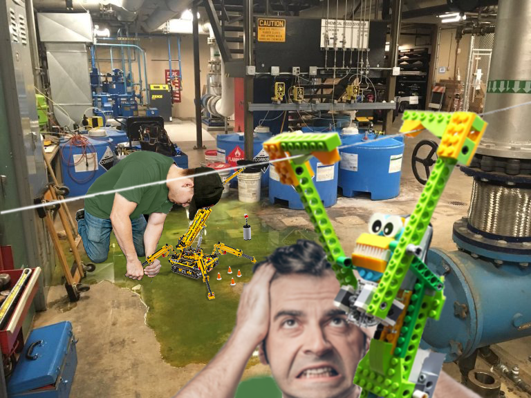 A green liquid is spilled out on the floor of a maintenance area. A worker kneels in the liquid, working on a LEGO Tehcnic crane. A different man appears frustrated as a LEGO Technic monkey crosses a string before him.