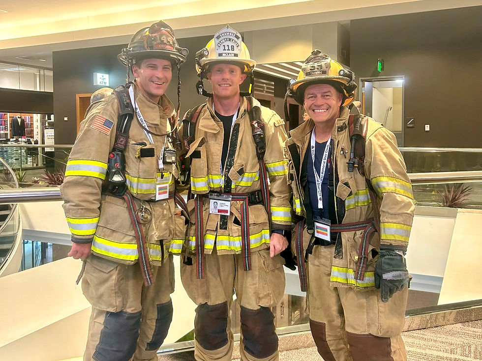 Three smiling Shawnee firefighters in tan gear and helmets pose indoors in a bright atrium, with names visible on helmet shields.
