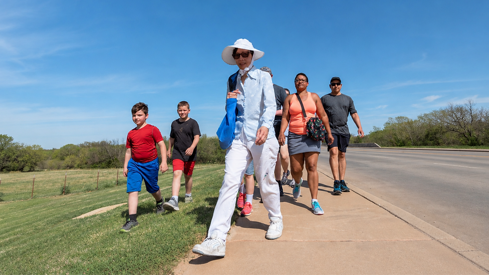 A group of Shawnee, Oklahoma residents, including kids and adults, walking on a paved path in Pottawatomie County. A sunny day with a blue sky and green grass.