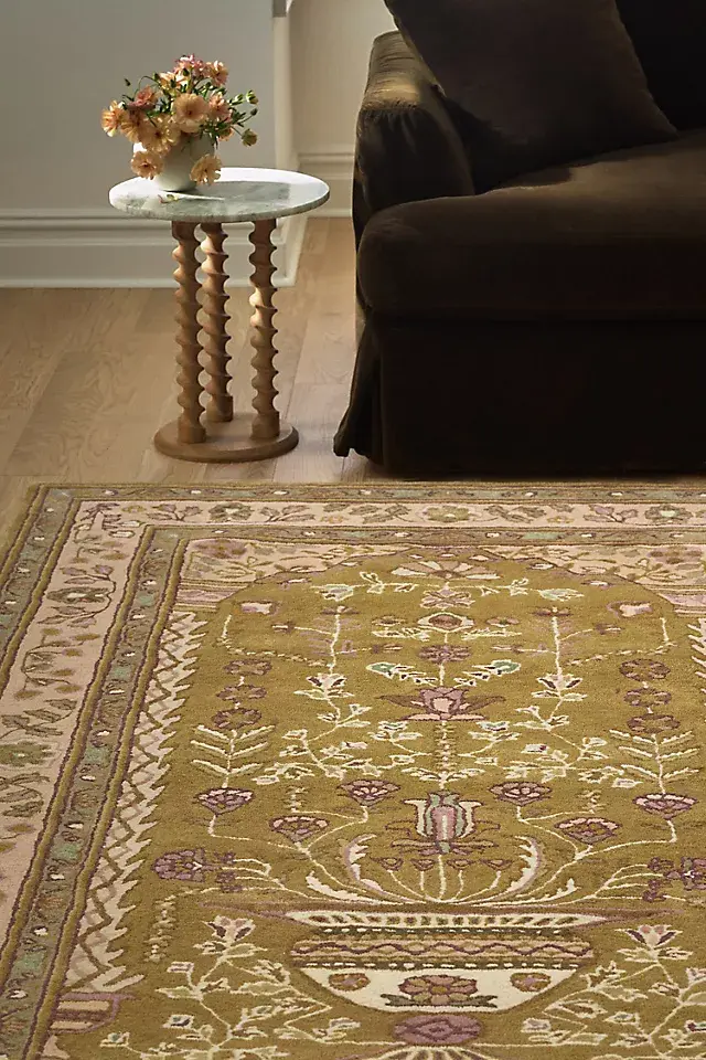 Cozy living room with a dark sofa, marble-topped side table holding flowers, and a patterned green rug on wood floor.