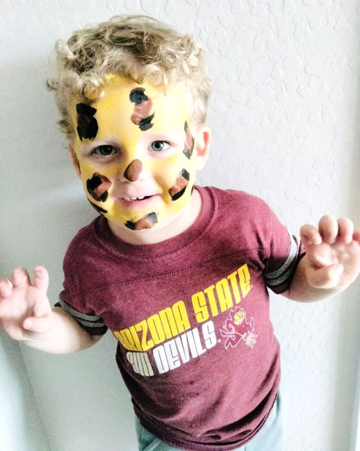a baby boy wearing maroon shirt has yellow and paint on his face