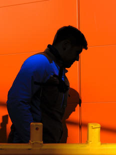 Mann im Arbeitsanzug und Schatten vor roter wand