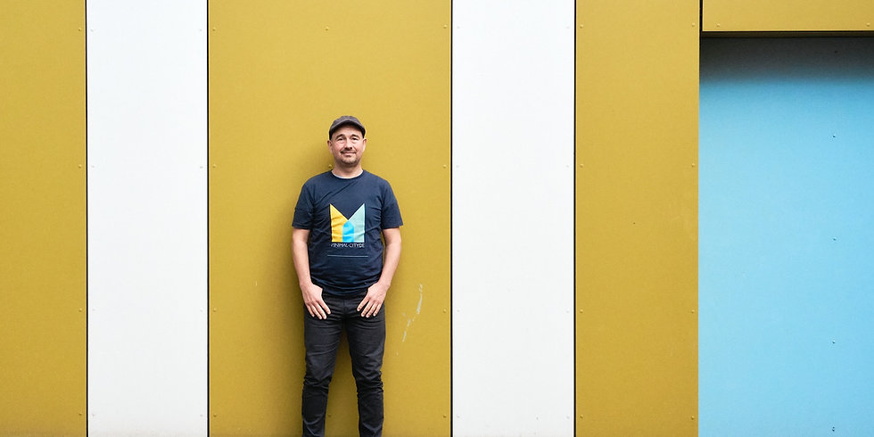 Portrait von Guido Klumpe im T-shirt mit Minimal-city-Logo vor eine bunten Wand