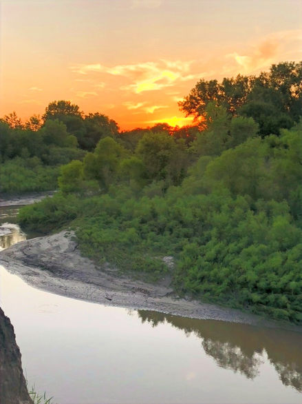 Scenic view of the Little Nemaha River during sunset, with vibrant orange hues reflecting on the water, creating a tranquil atmosphere at Little River's Edge RV Park and Campground