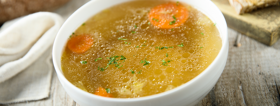 Bowl of homemade clear broth soup with carrot slices and fresh parsley on top, served with bread on a rustic wooden table.