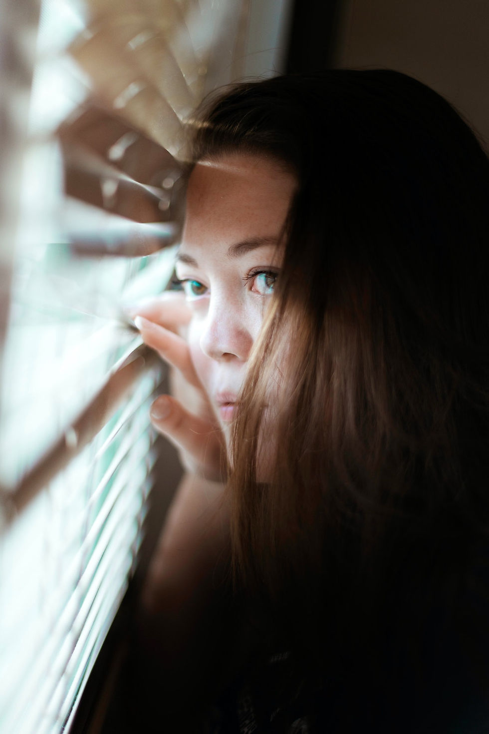 A woman peering out from behind venetian blinds