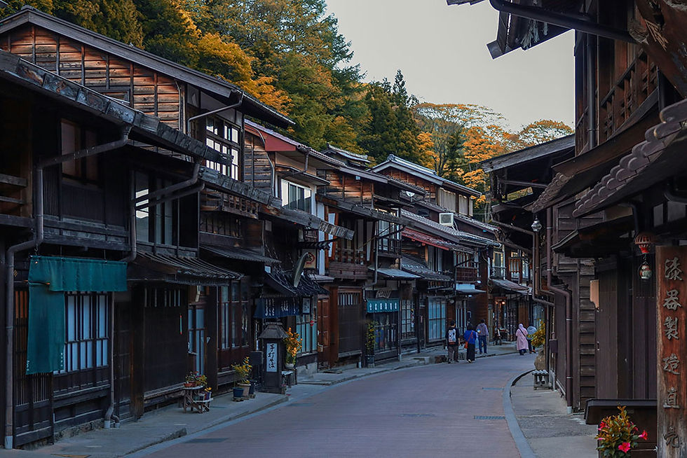 A serene view of a traditional Japanese street lined with historic wooden buildings, set against a backdrop of vibrant autumn foliage.
