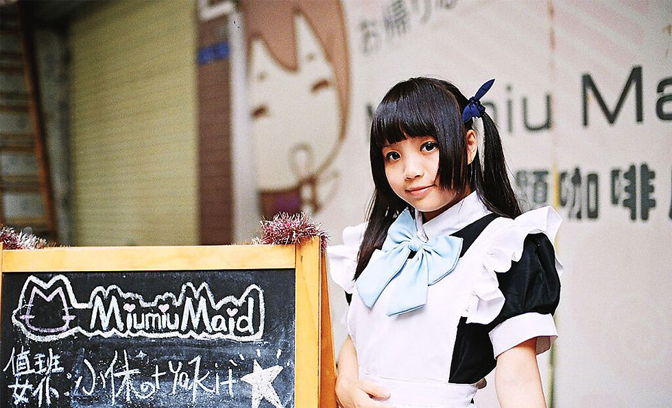 A young woman in a maid outfit poses beside a chalkboard sign at Miumiu Maid Café, featuring a cute cat illustration and adorned with festive decorations.