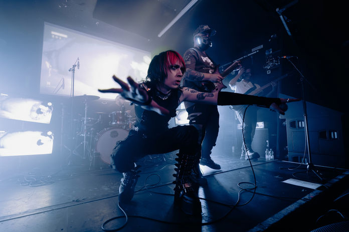 A singer of Nightlives crouching on the floor with his arms out, and fingers close to the camera