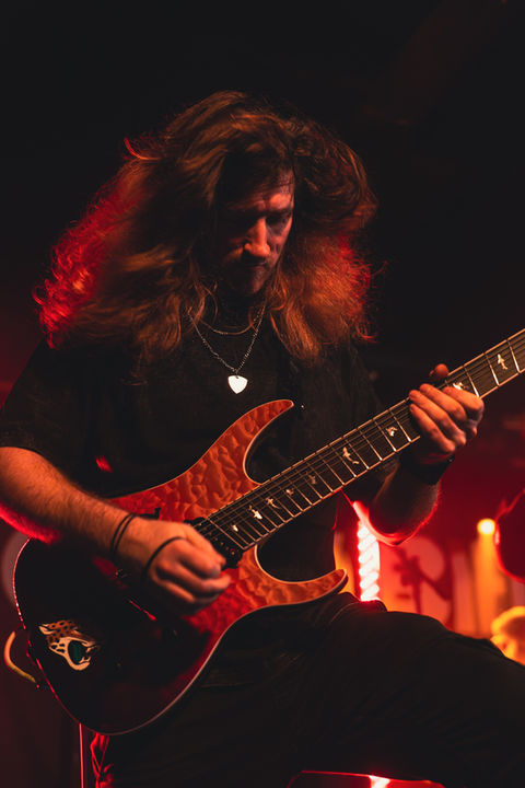 A guitarist in Struggler with an orange background playing the guitar and his hair swaying