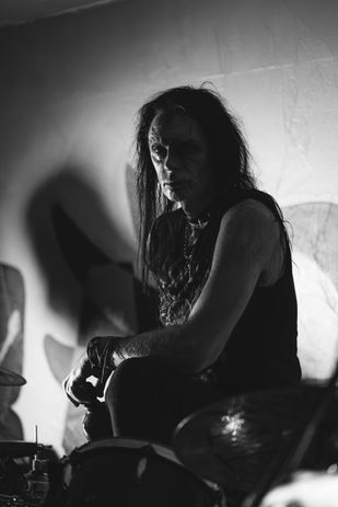 A drummer in The Shallow souls live looking at the camera and standing in front of the crowd, with the image being black and white