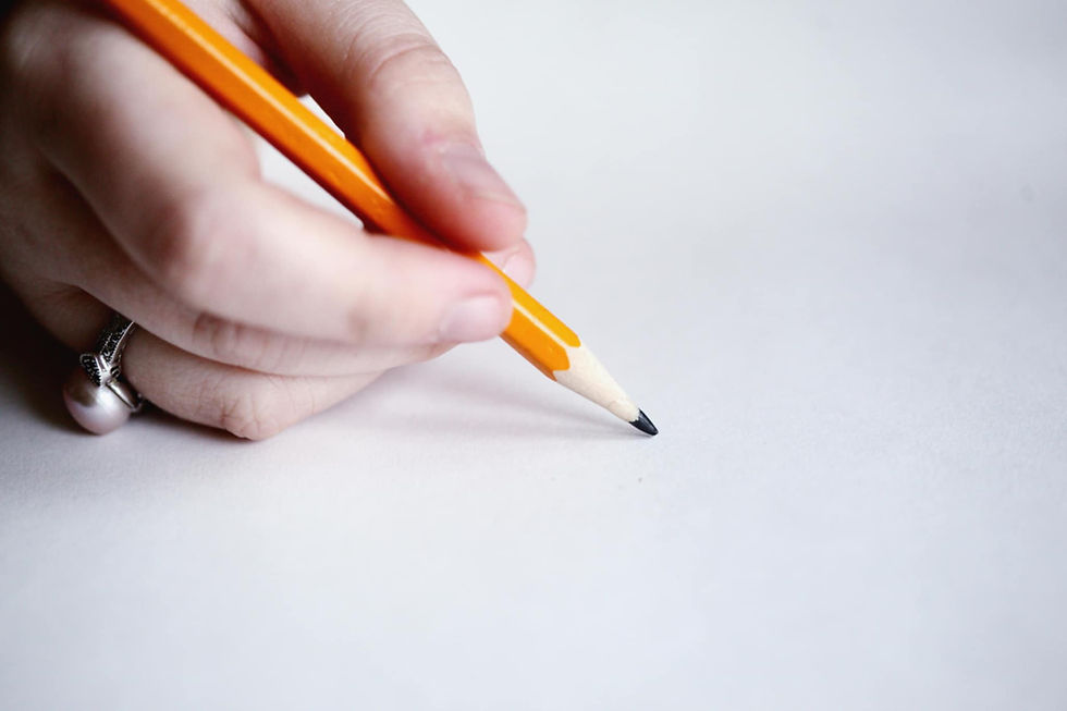 Hand holding a yellow pencil poised to write on a blank white paper. Minimalist setting with a silver ring visible on the hand.
