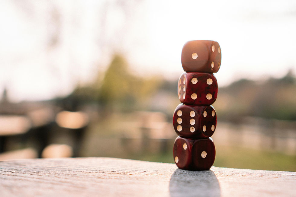 Five red dice are stacked on a wooden surface outdoors in soft focus. Warm sunlight creates a gentle, calm atmosphere.